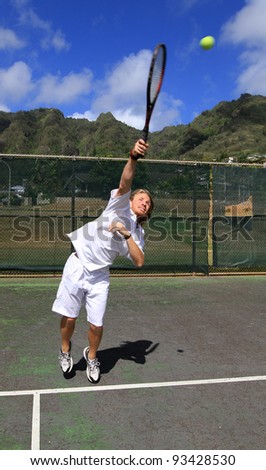 A handsome blonde tennis player serves the ball over the net with confidence