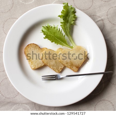 White dish with three heart shape chips and two lettuce leaves and a small fork