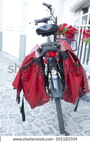 Bicycle with red pannier bags parked outside the front door of a house on a street in Bruges, Belgium.