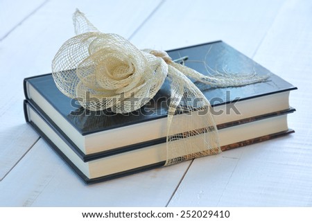 Two books tied with a raffia ribbon and decorated with an artificial flower on an old white wooden table