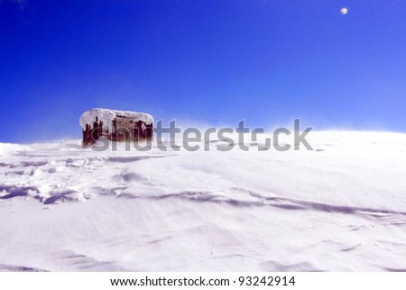Cottage on a mountain slope in winter, with rabbit tracks in snow in the foreground