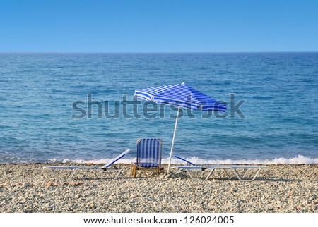 Sun umbrella and sunbeds in front of a blue sea and sky