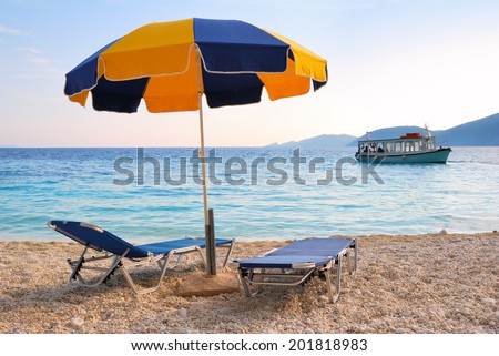 Colorful sun umbrella and two sunbeds with a blue sea and a boat