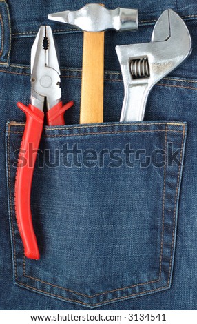 Toolkit of hammer, adjustable spanner and combination pliers in a blue jeans pocket