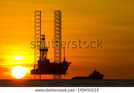 Silhouette of an offshore drilling rig and supply vessel at an orange sunset