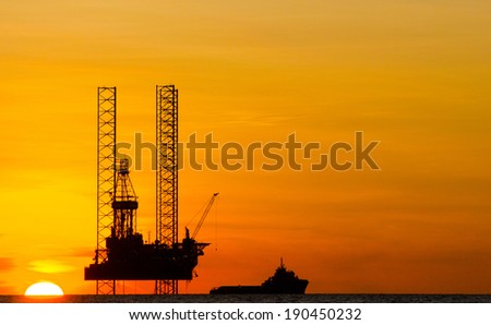 Silhouette of an offshore drilling rig and supply vessel at an orange sunset