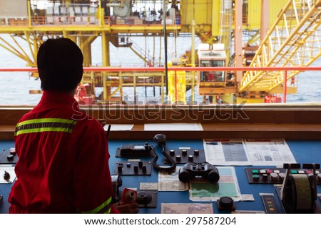 A helmsman on the bridge of a supply vessel nearby an offshore oil-rig