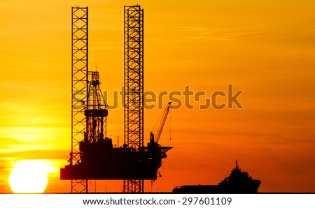 Silhouette of an offshore drilling rig and supply vessel at sunset