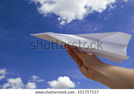 Female hand holding paper airplane against blue sky