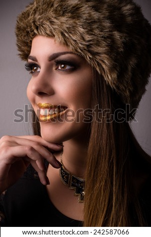 Vivacious smiling winter fashion model in a fur hat and knitwear looking to the side with her hand to her chin, close up face portrait