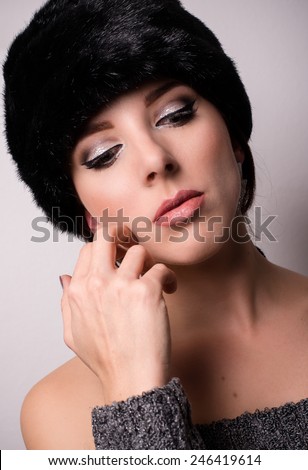 Close up Thoughtful Pretty Woman Wearing Furry Bonnet, Looking Down with Hand Touching her Face. Captured with Light Brown Background.