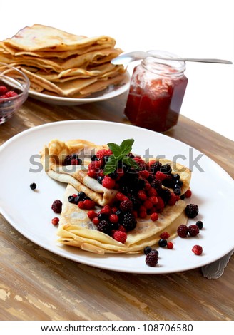 plate with fresh berries and pancakes filled with homemade jam placed over a napkin