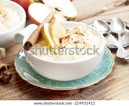 Rice Pudding with Apple Slices and Cinnamon Spice Sticks on Wooden Background