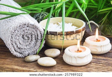 Natural Spa Setting with Green Leaves and Burning Candles, Towel and Rocks, Bamboo Bowl with Water on Wooden Background