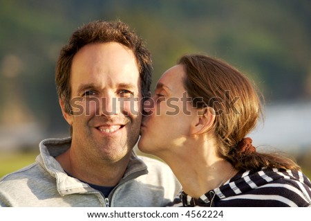 Loving couple outside, the wife is giving her husband a kiss on the cheek