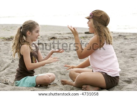 Cute girls playing a clapping game at the beach in the sand