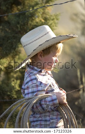 Cute little boy dress in his cowboy gear holding a rope outdoors