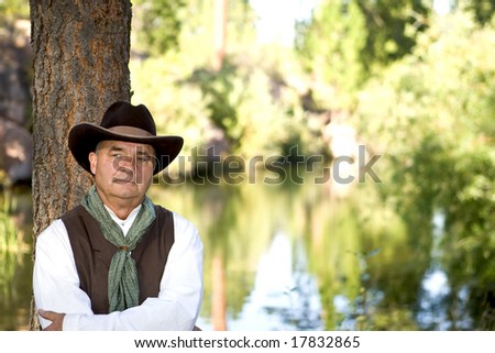 Handsome older cowboy chewing on some hay, leaning against a tree