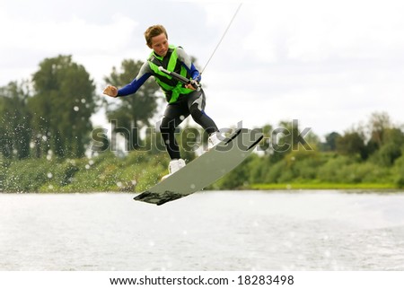 Teen in wetsuit catching air wake-boarding with a cute expression on his face