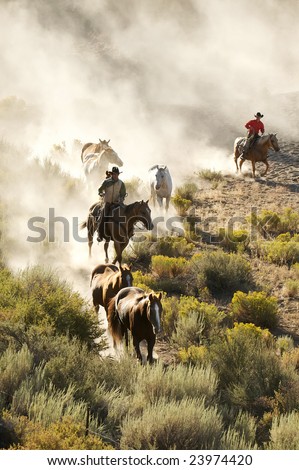 Two cowboys guiding a line of horses through the desert