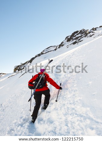 Woman skier with skis on backpack, climbing up a boot packed trail.