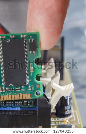 Human finger guides a memory module into the slot on the mother board.