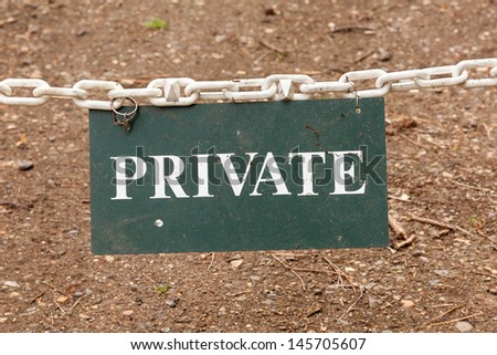 A Private property sign suspended on a white chain forming a barrier.