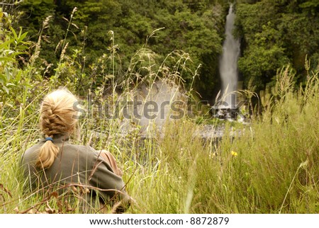 Woman seating in tall grass watching a waterfall