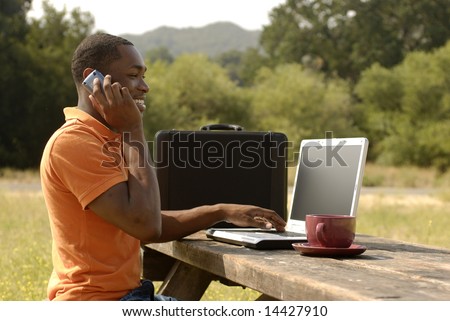 African American man speaking on the phone while working on laptop computer