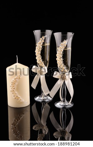 glass with champagne, candle and boxes for wedding rings on black background