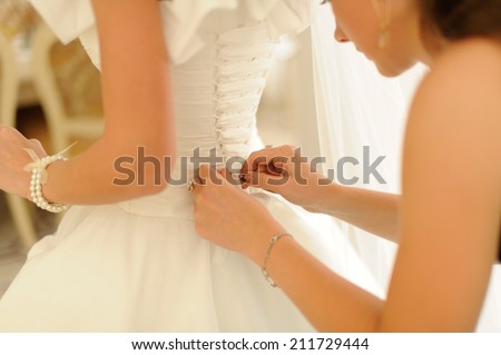Bridesmaid is helping the bride to dress