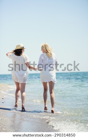 happy girls in white dresses  running on the sea beach