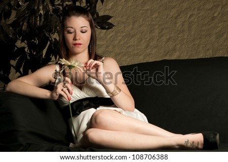Sad and depressed beautiful young woman lounging on couch picking daisy petals, he loves me, he loves me not