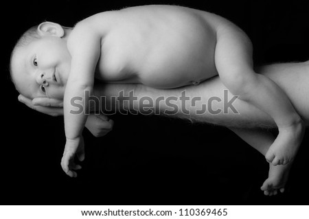 black and white photo of newborn baby held on father's arm and hand on isolated black background