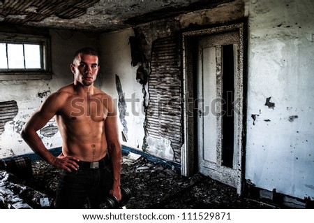 Attractive young man in grunge abandoned house with rippling abs and barbell