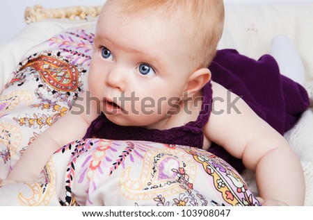 fashion baby girl lying on a beautiful fabric in the basket and looks to the side on a white background.