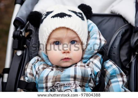 cute healthy little boy with amazing blue eyes, dressed in a checkered blue overalls sat in a wheelchair and surprised looks in the open air