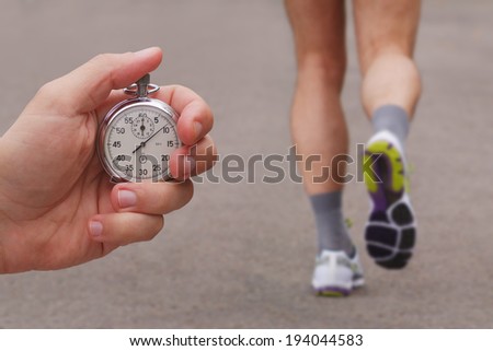 Old stopwatch in a hand and blurred runner athlete feet running on a road