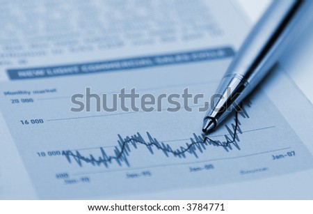 Gold and silver pen pointing to graph indicating business and financial trend, in a magazine or report.