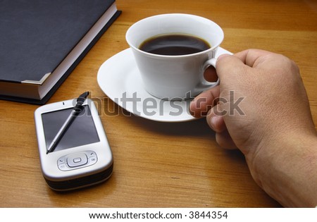 Office scene with a diary, a PDA and an executive picking up a cup of coffee