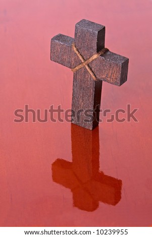 A wooden cross reflecting on a reddish wooden table. Perfect for use in christian, religious, eater or christmas themes.