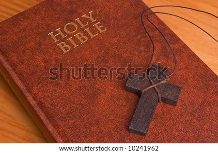 The Holy Bible, closed on a table, with a wooden cross on it. Perfect for use with any religious theme.