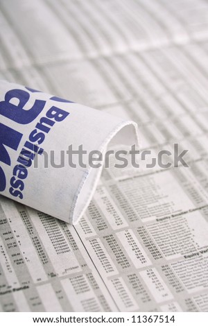 A rolled up mewspaper with the word business om it, placed over share prices.