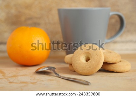 A pile of round cookies near a cup of milk and an orange on a wooden table
