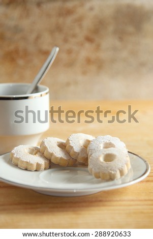 Saucer with italian canestrelli biscuits sprinkled with icing sugar near a white cup.