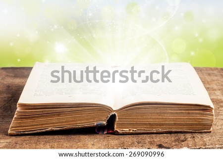 Open book on a wooden table with light effects on a green background