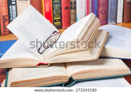 Stack of open books and glasses on the desk in the library