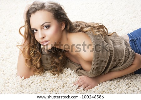 pretty and attractive young brunette in a warm brown sweater laying down on a white carpet, she looks in to the lens with sensual expression,  her right hand is near the face and the left hand is on