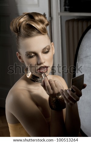 fashion portrait of cute and elegant woman applying makeup on backstage with spot light on her face