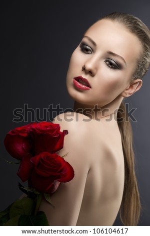 pretty blonde girl\'s low key portrait with three red roses, her body is turned in profile, her face is turned of three quarters and looks down at right